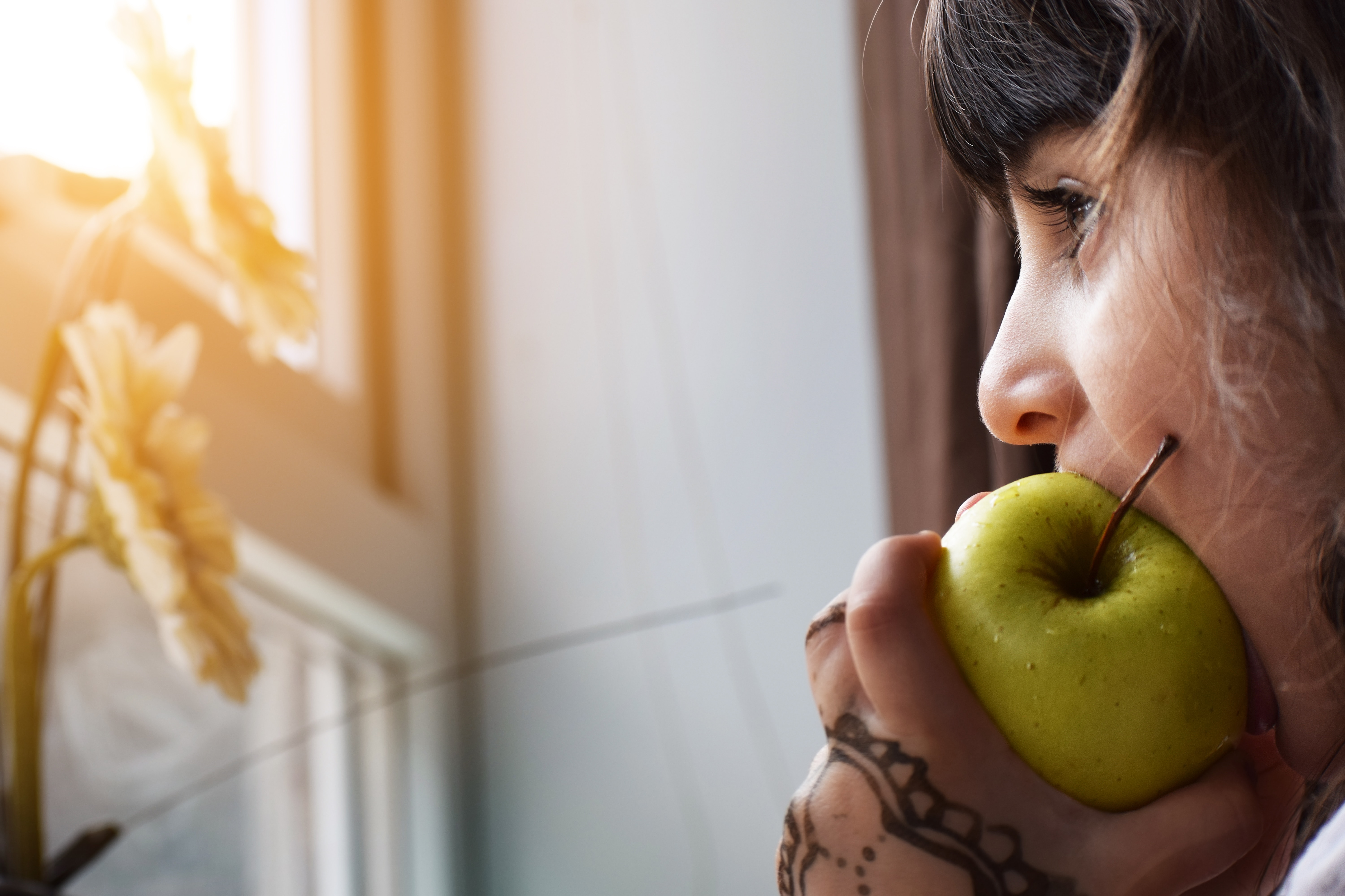 young woman eating a green apple while looking out a window